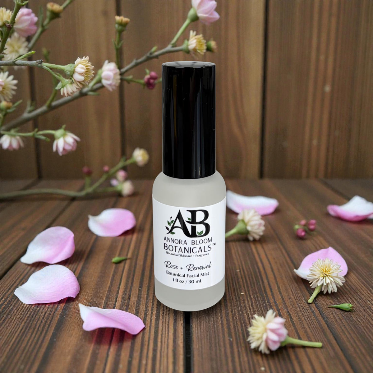 Bottle of Anora Bloom Botanicals rose facial mist product on a wooden surface with flowers and petals.
