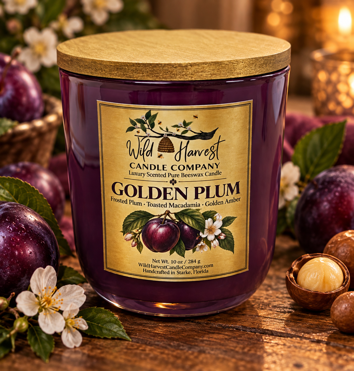 A Wild Harvest Candle Company 'Golden Plum' scented candle in a dark purple glass jar with a gold lid, styled on a rustic wooden table with fresh plums, white blossoms, and nuts.
