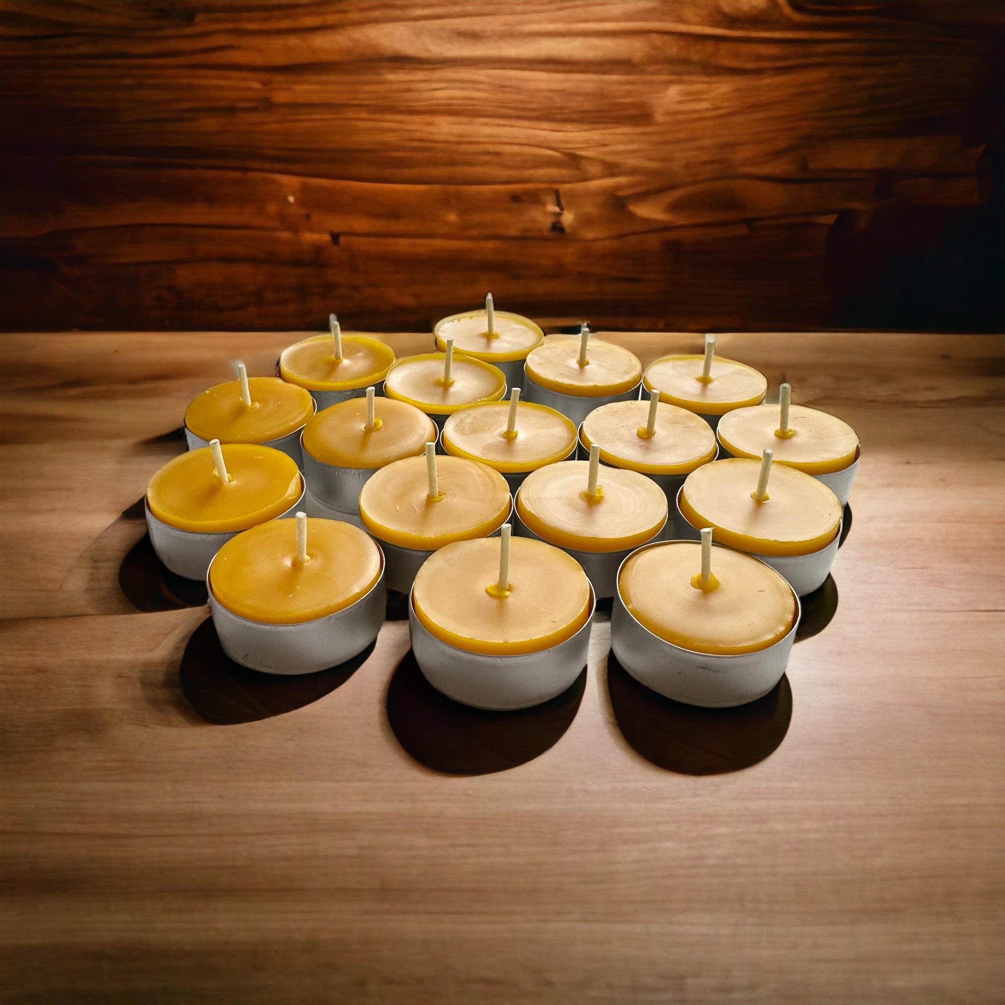 several pure beeswax tea light candles in aluminum cups on a wood table with a warm background.