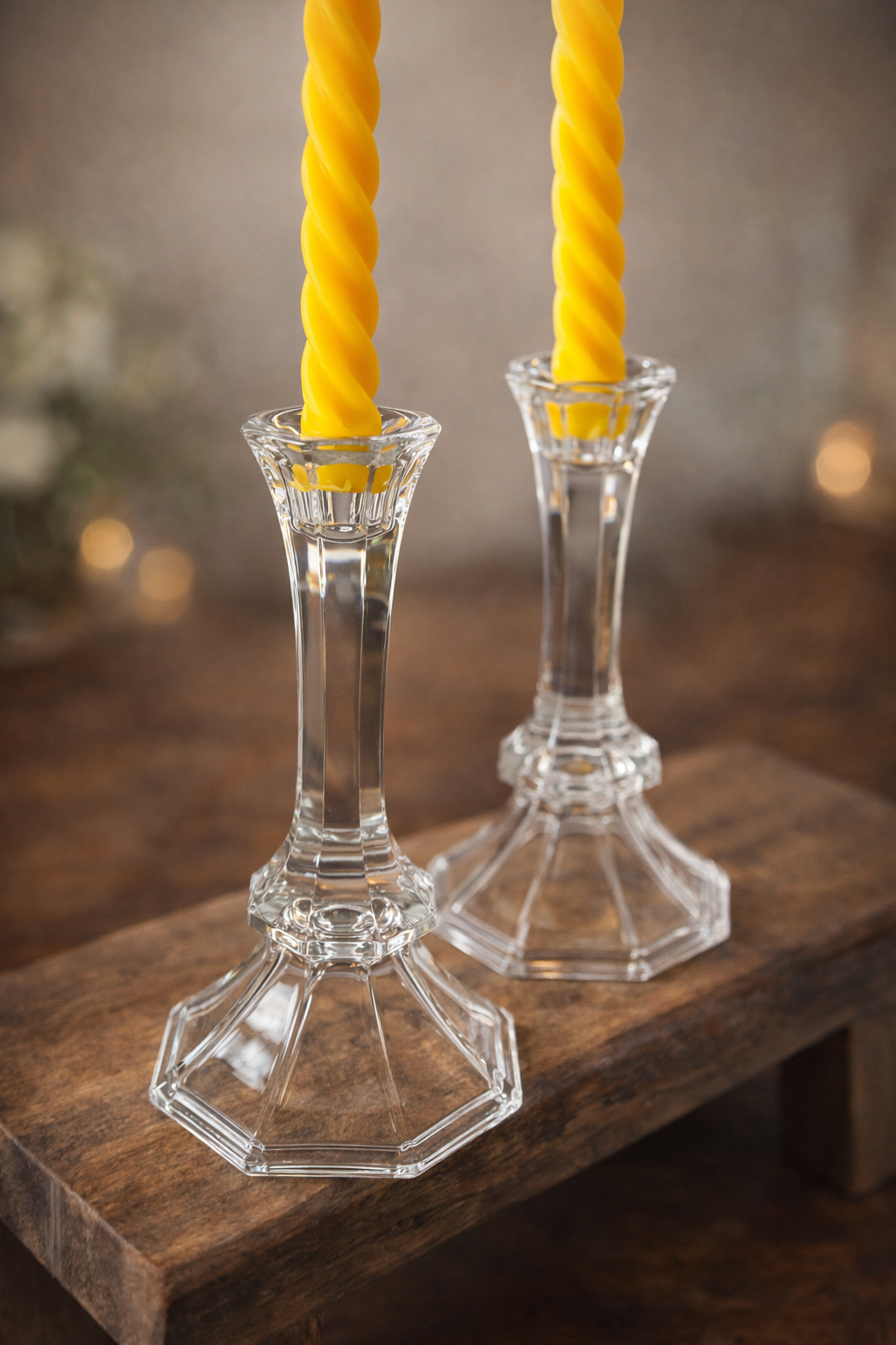 Clear glass candlestick holders with yellow candles on a wooden surface.