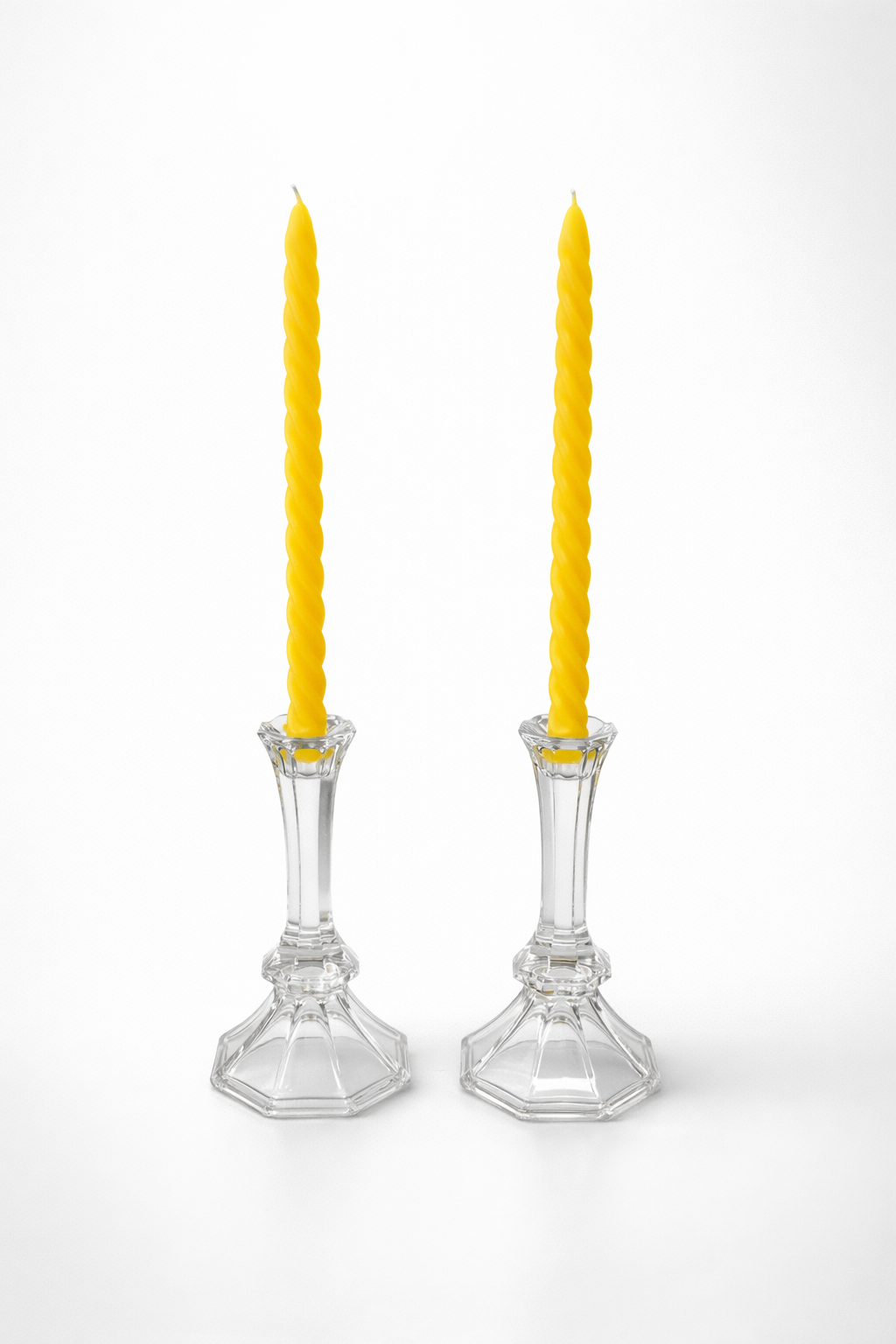 Two clear glass candlesticks with yellow candles on a white background
