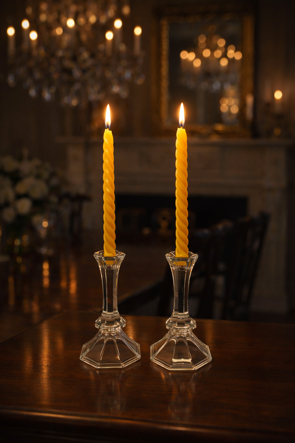 Two lit yellow candles in glass candlesticks on a wooden table with a blurred background