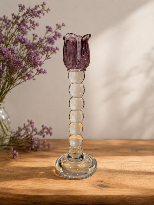 Glass candle holder with purple tulip style top on a wooden surface with a blurred background