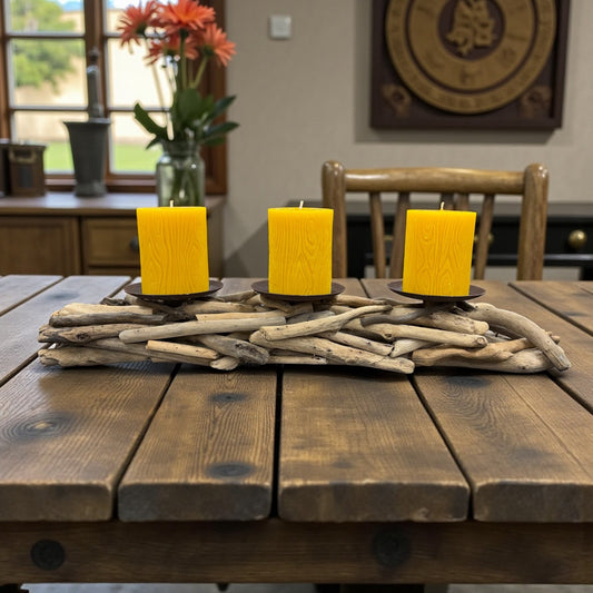 Three yellow candles on a wooden table with driftwood, in a room with a window and decorative items.